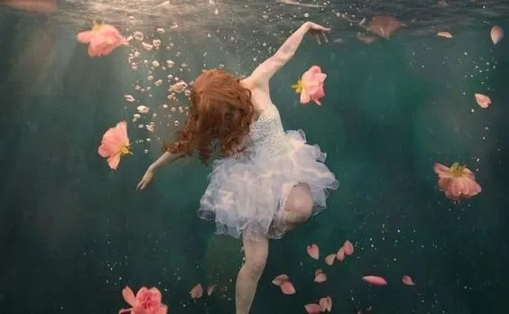 Una mujer con vestido blanco flota bajo el agua entre flores, para el curso sobre La insoportable levedad del ser de Milan Kundera